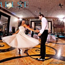 Image of bride and groom dancing in ballroom reception space with guests all around